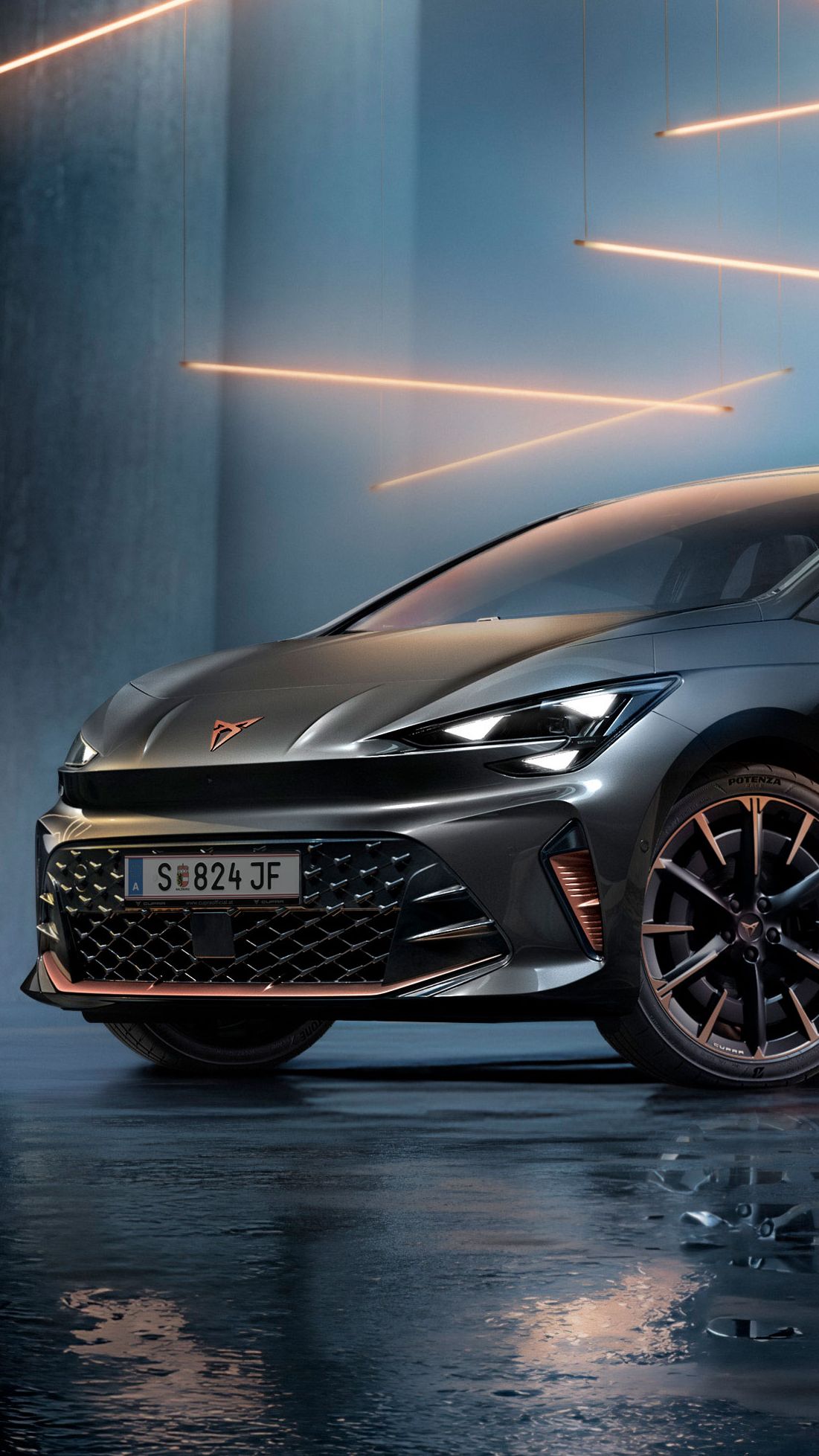 Ein grauer CUPRA Born steht in einer modernen, dunklen Umgebung mit vertikalen Säulen und leuchtenden LED-Streifen. Der Boden ist glänzend und reflektiert das Fahrzeug sowie die Beleuchtung. Das Auto wirkt kraftvoll und elegant.