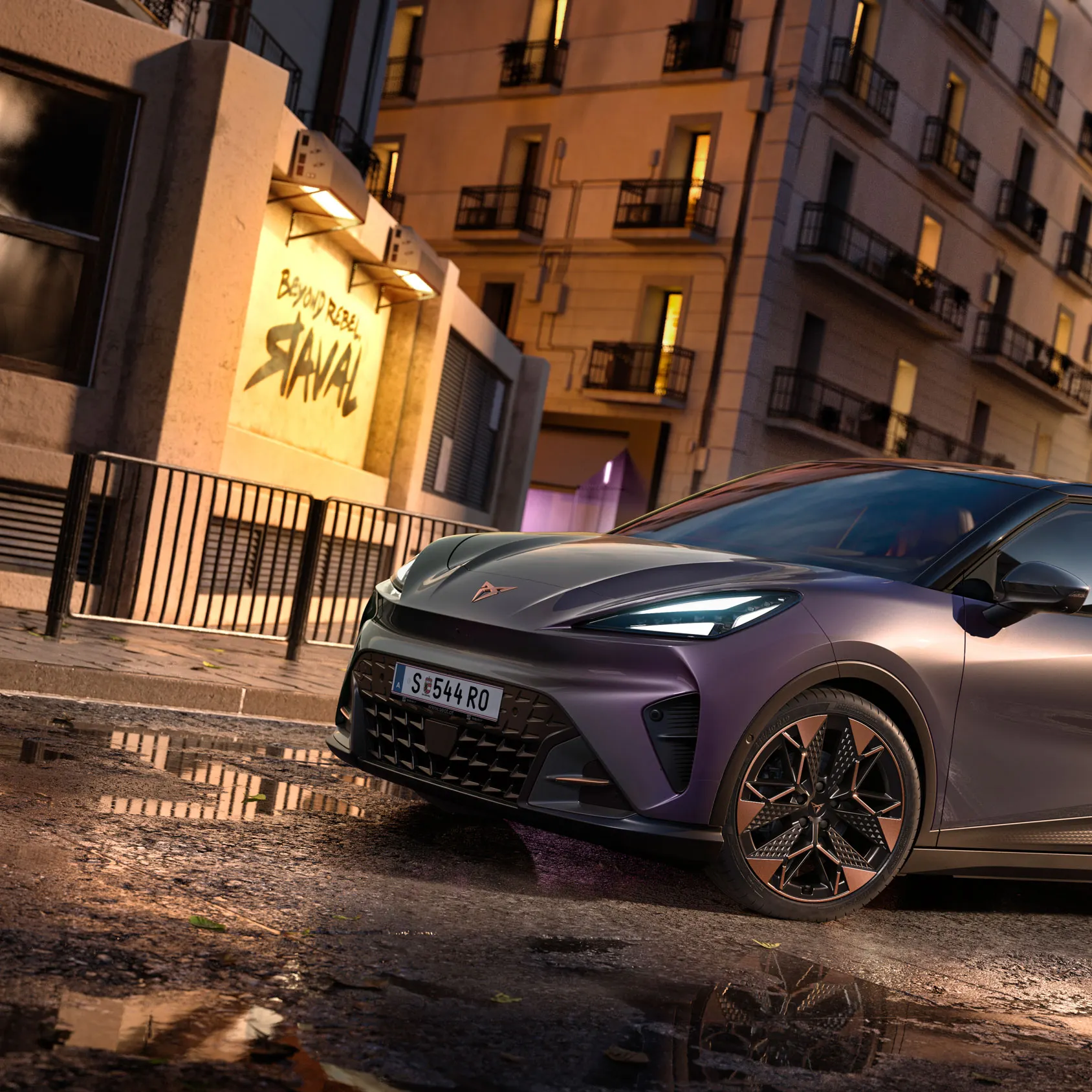 Vůz CUPRA Raval v barvě Plasma se střechou Manhattan Grey stojí v moderním industriálním prostředí. Přední tříčtvrteční pohled zvýrazňuje ostré linie karoserie, měděná aerodynamická kola a osvětlené logo CUPRA. V pozadí je výrazný nápis „Raval“, který podtrhuje identitu tohoto elektrického městského vozu.